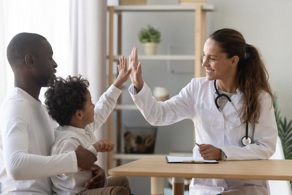 a physician high-fiving a child patient in a doctor's office