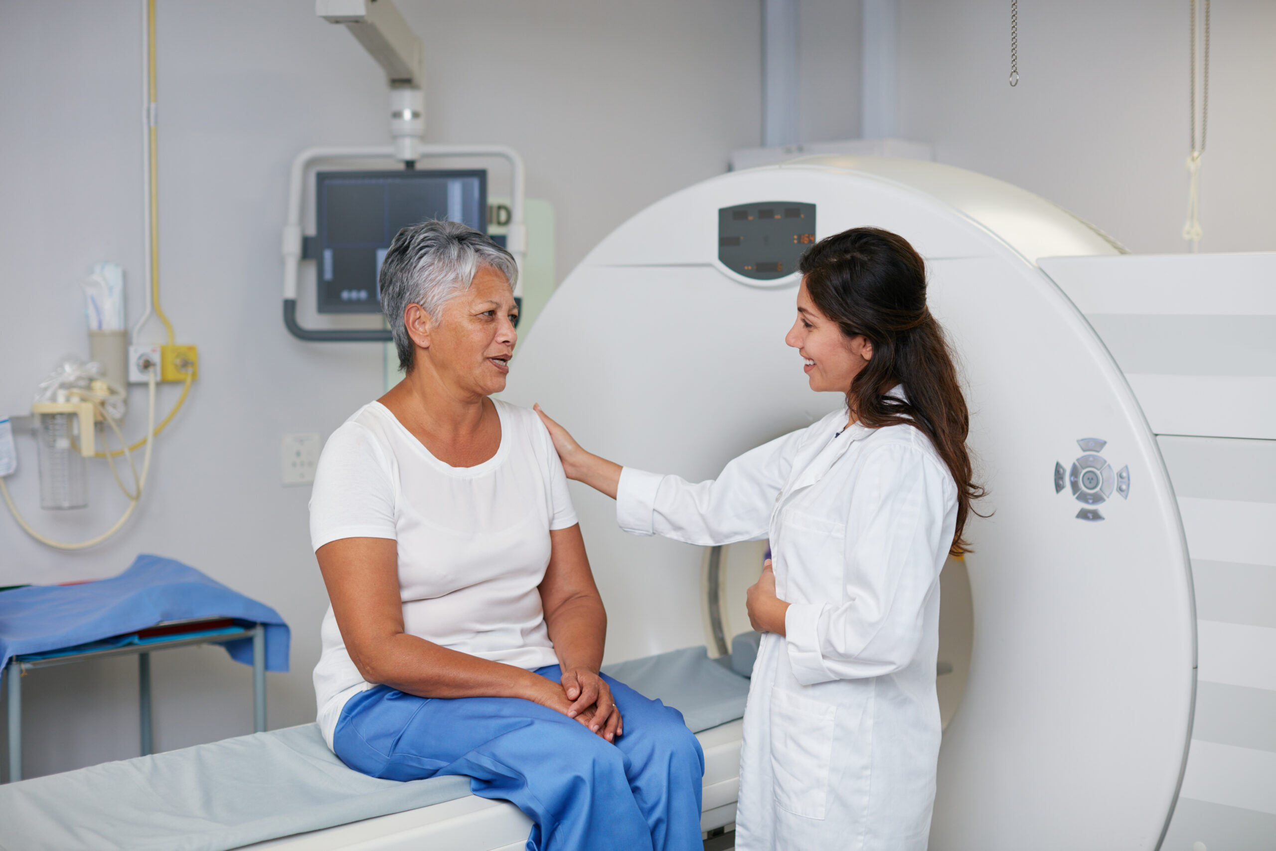 physician comforting an adult patient who is sitting on an MRI table